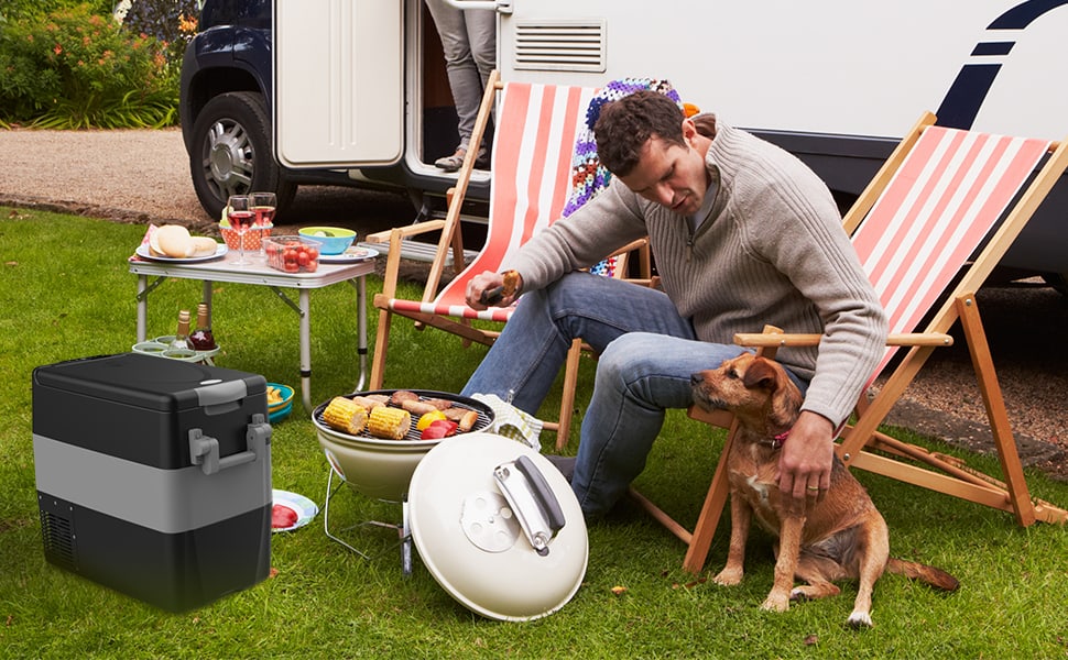 A guy using his camping fridge and grill to set up lunch for his family and puppy at their campsite