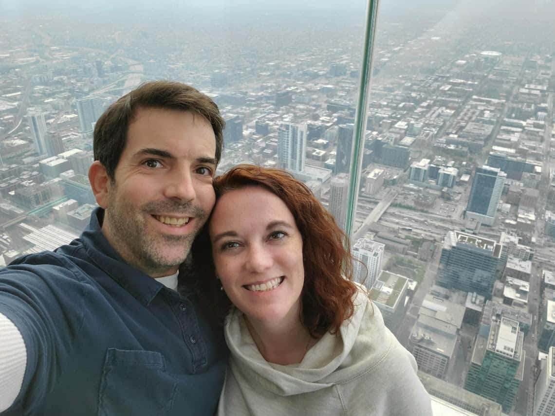 Darcee and Eric sitting on the glass overhang from the top floor of the Skydeck of Willis Tower in Chicago 